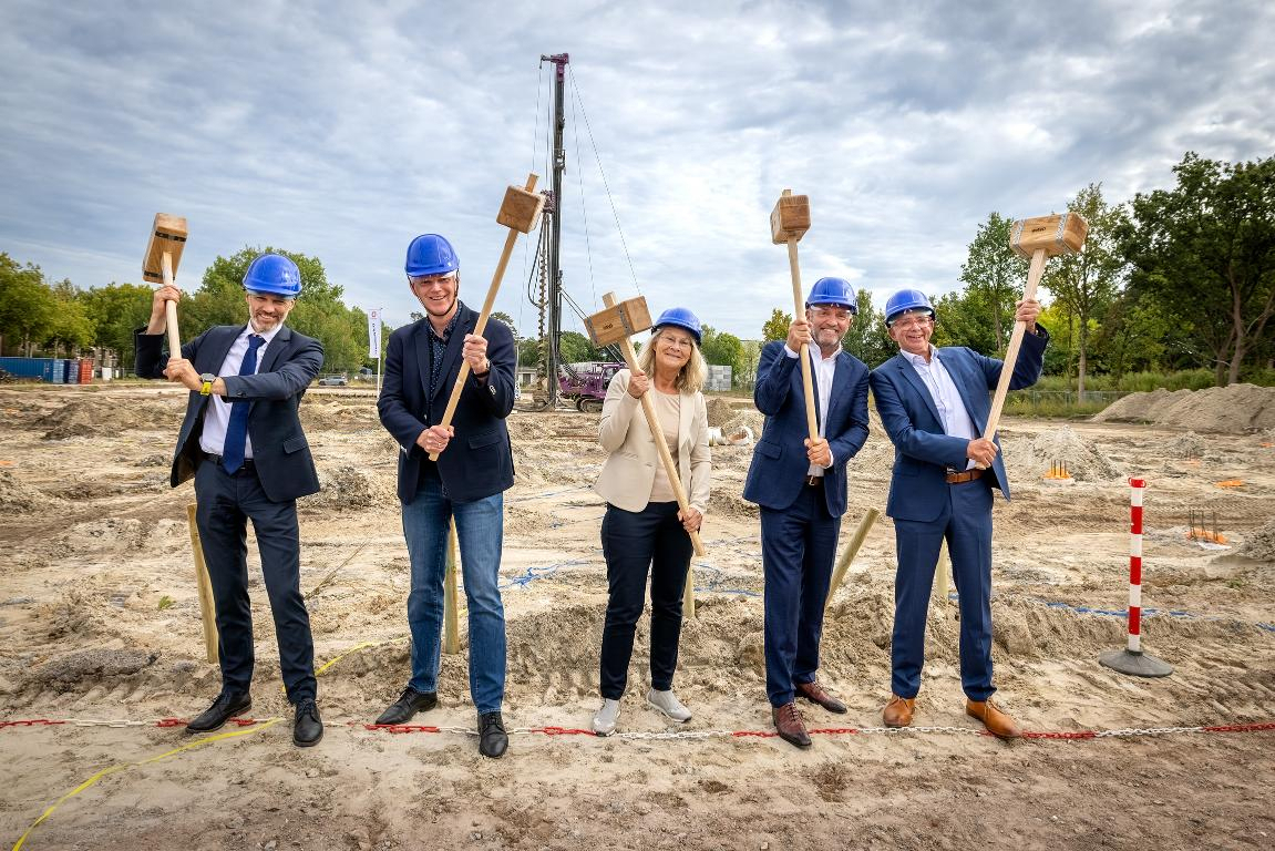 5 samenwerkende partijen met een hamer in de hand om de laatste heipaal de grond in te slaan op circusterrein