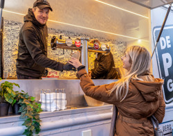 man overhandigt frietje vanuit frietkar aan vrouw